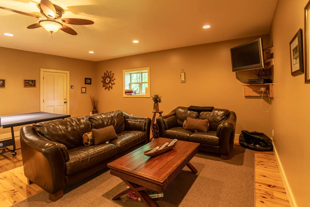 This image presents a comfortable entertainment area with leather couches set around a wooden coffee table, facing a television. The cozy, inviting mood suggests a perfect spot for family movie marathons and casual board games.
