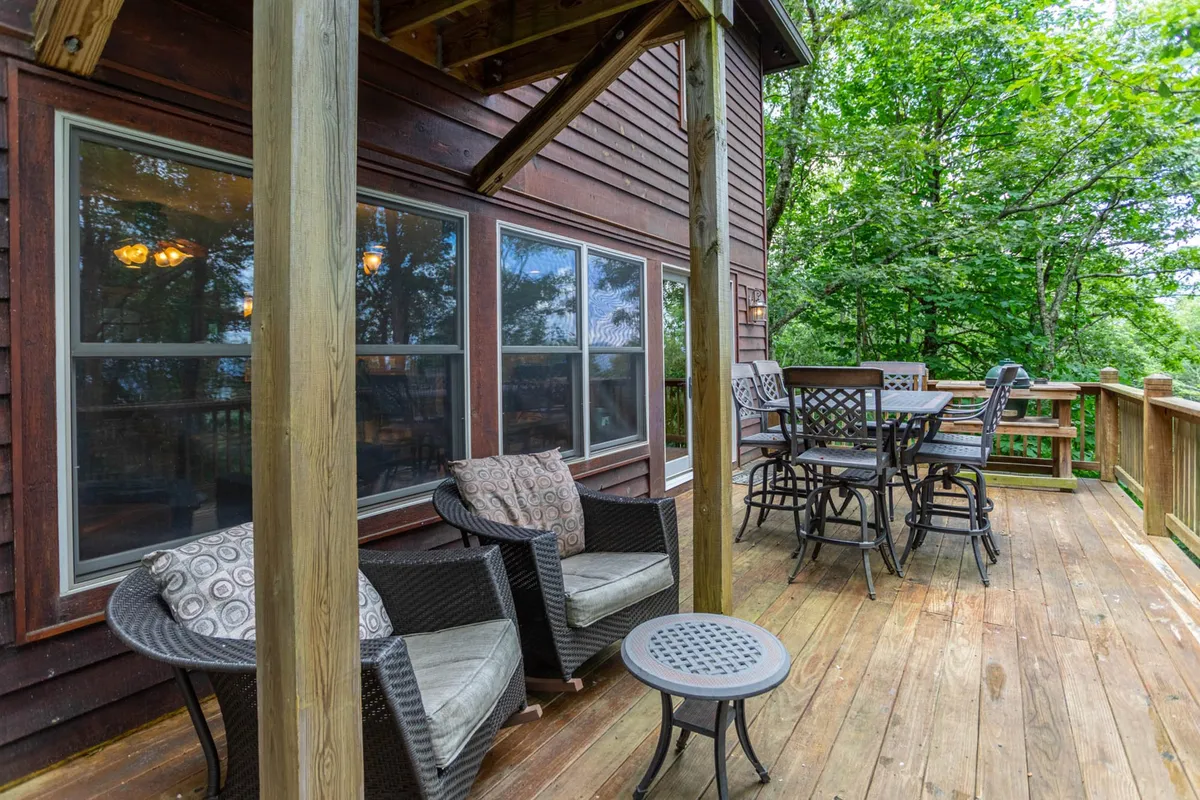 The photo features a comfortable outdoor seating area with a bar-height dining table, set against a backdrop of lush greenery. The space invites guests to enjoy meals, morning coffee, or quiet moments with loved ones in the fresh mountain air.